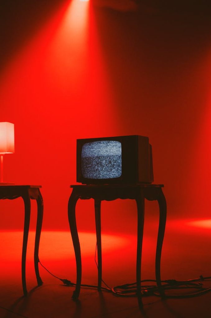 Retro TV displaying static on wooden table under dramatic red lighting.